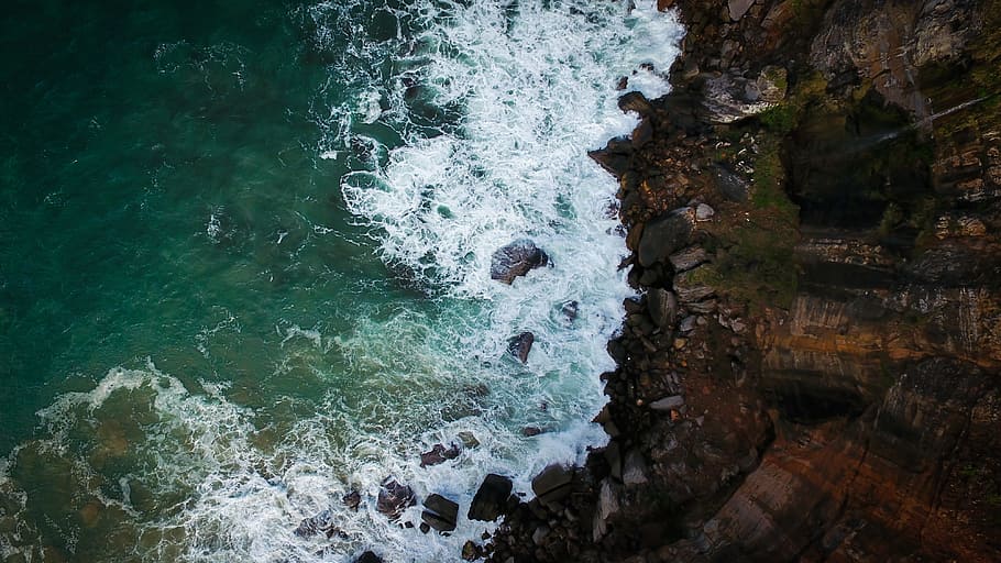 aerial photography of brown cliff near body of water, aerial view of body of water waves near rock formation HD wallpaper