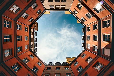 low-angle photography of hexgonal orange and brown concrete building under white clouds and blue sky during daytime, low angle photo of red brick building under blue skies forming a hexagonal pattern HD wallpaper