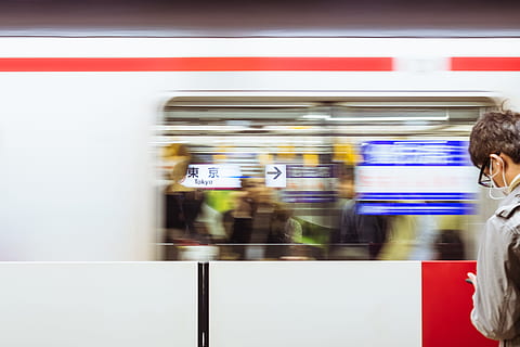 A blurry shot of a moving train in front of a man at the Tokyo Station., man standing in front of moving train while wearing white earbuds and using smartphone HD wallpaper