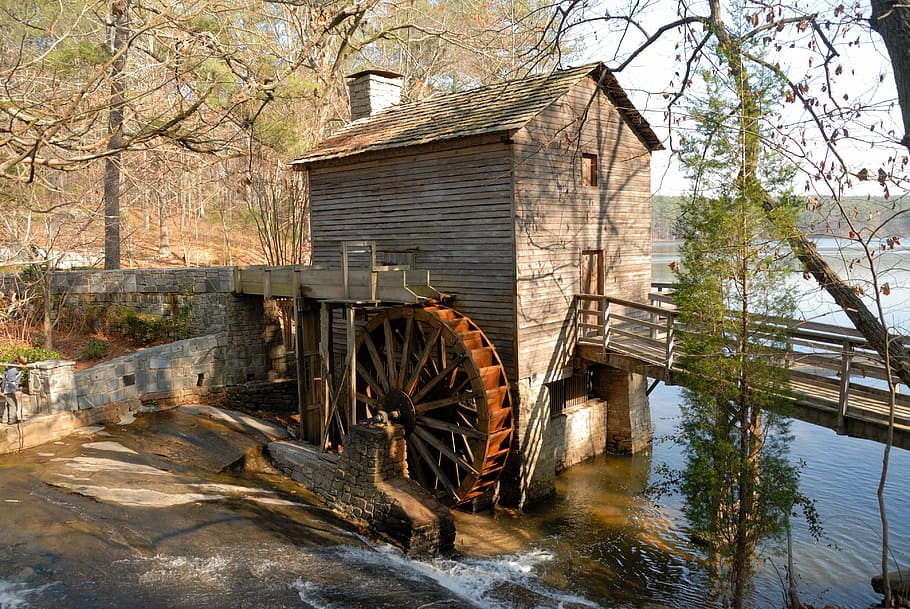 brown wooden watermill with wooden bridge under tree during daytime