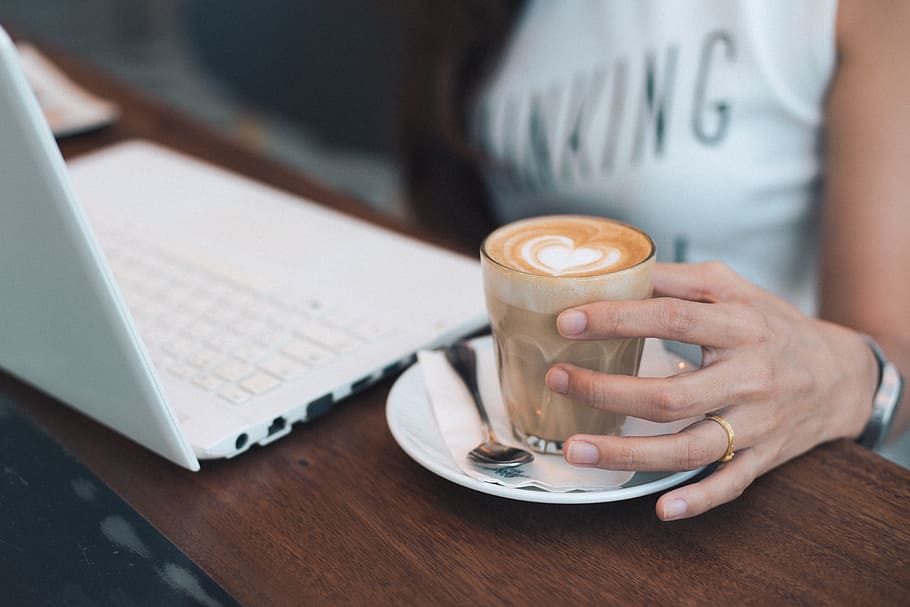 person holding glass cup with frappe beside white laptop computer HD wallpaper