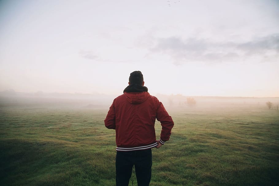 man in red full-zip jacket on green grass field during foggy day HD wallpaper