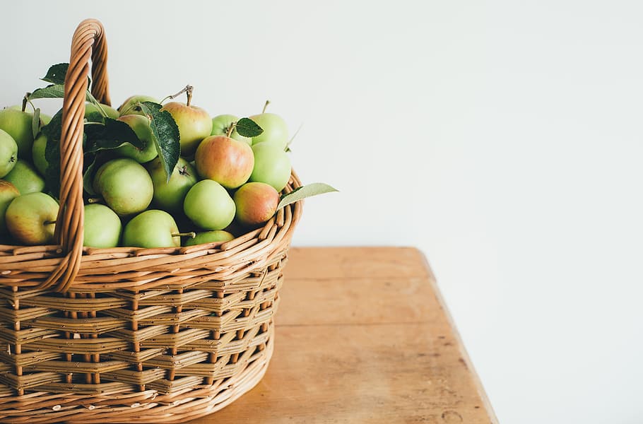green fruits in basket, brown wicker basket filled with apples on brown wooden desk HD wallpaper