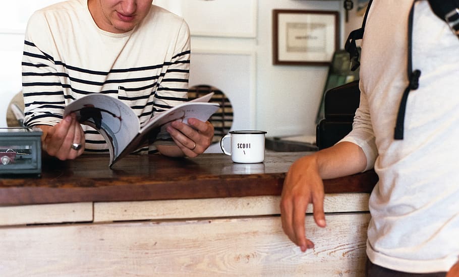 person leaning on table beside man holding book, people, counter HD wallpaper