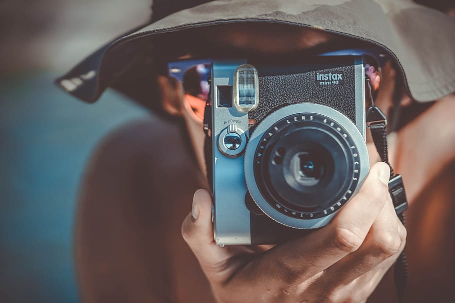 person with brown bucket hat using black and grey Fujifilm Instax camera, man holding grey and black Intax Camera HD wallpaper