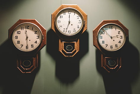 three brown framed white analog wall clocks hanging by wall, three brown pendulum analog clocks on gray wall HD wallpaper