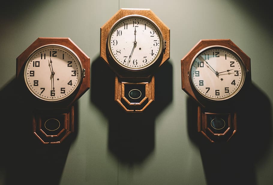 three brown framed white analog wall clocks hanging by wall, three brown pendulum analog clocks on gray wall HD wallpaper