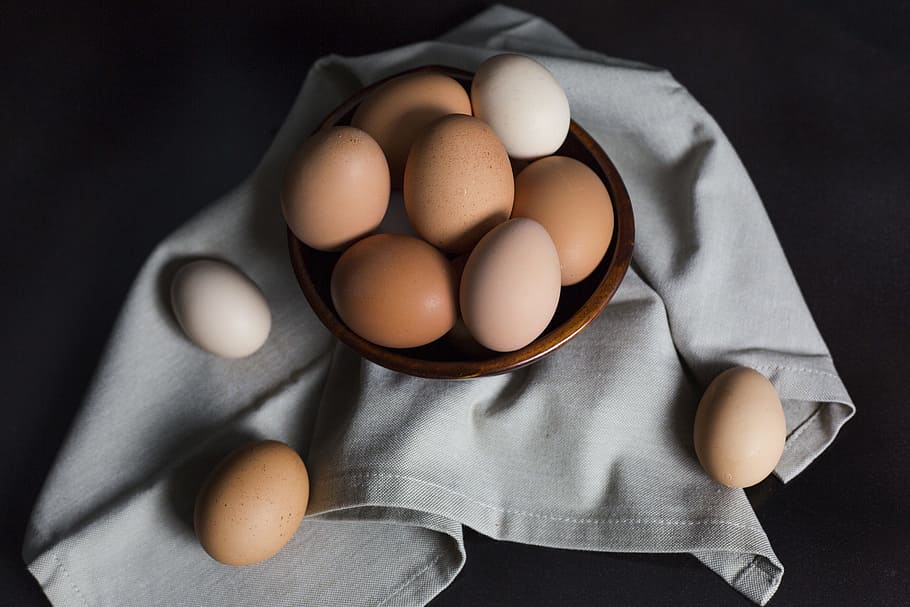 beige and white eggs on brown wooden bowl, brown and white eggs on brown bowl