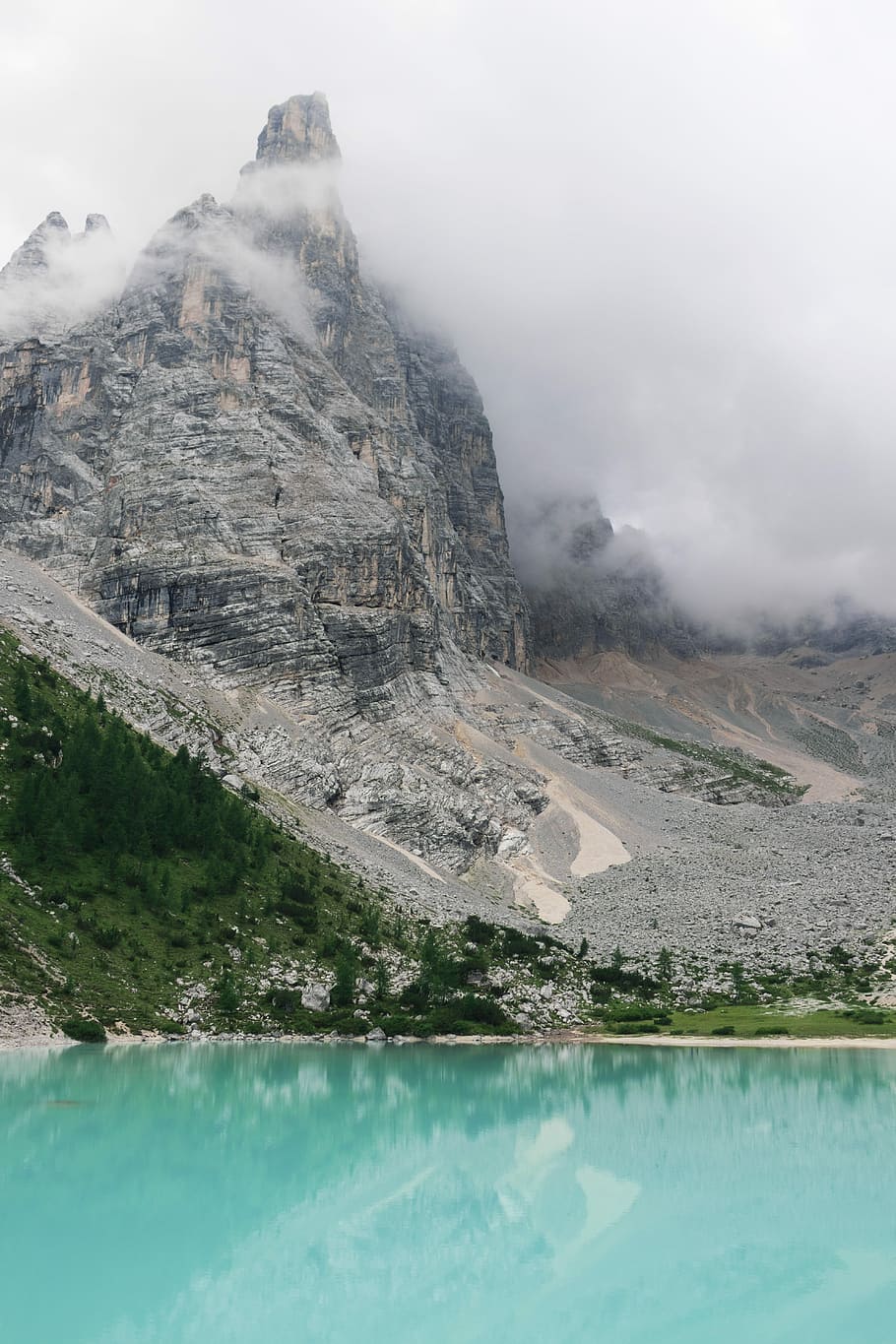 body of water at the foot of the mountain surrounded by clouds, gray and brown rock formation under cloudy sky