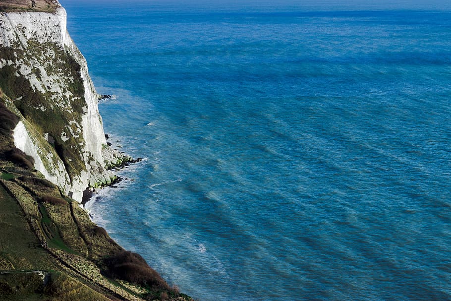 aerial photography of mountain cliff beside seashore during daytime, mountain cliff and body of water HD wallpaper