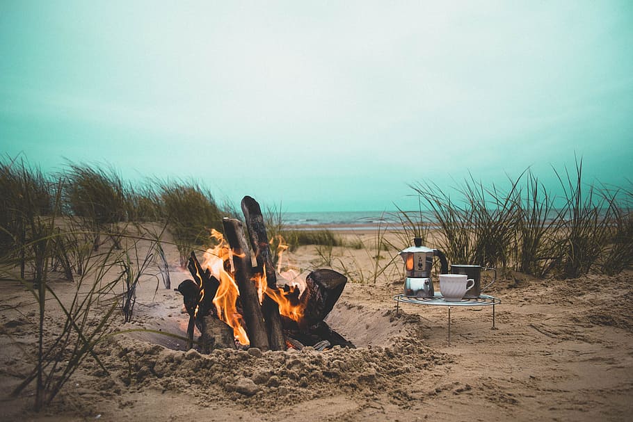 fireplace near cup and pitcher on desert, bonfire beside seashore during daytime HD wallpaper