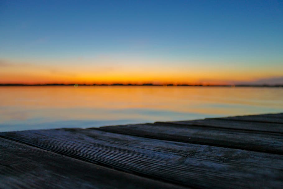 selective focus photo of brown wood planks in front of beach during golden hour, dock and overlooking body of water during golden hour