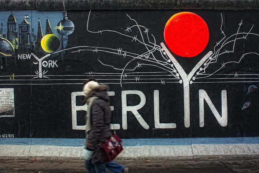 person walking on road against mural painted wall, east side gallery