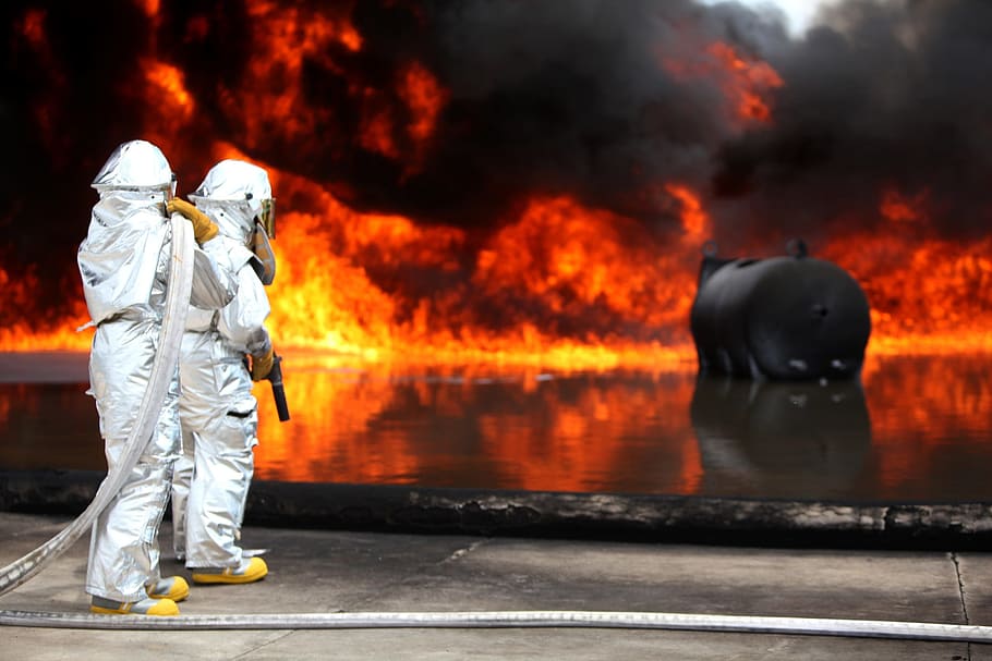 firefighters standing on concrete platform facing burning tank, HD wallpaper