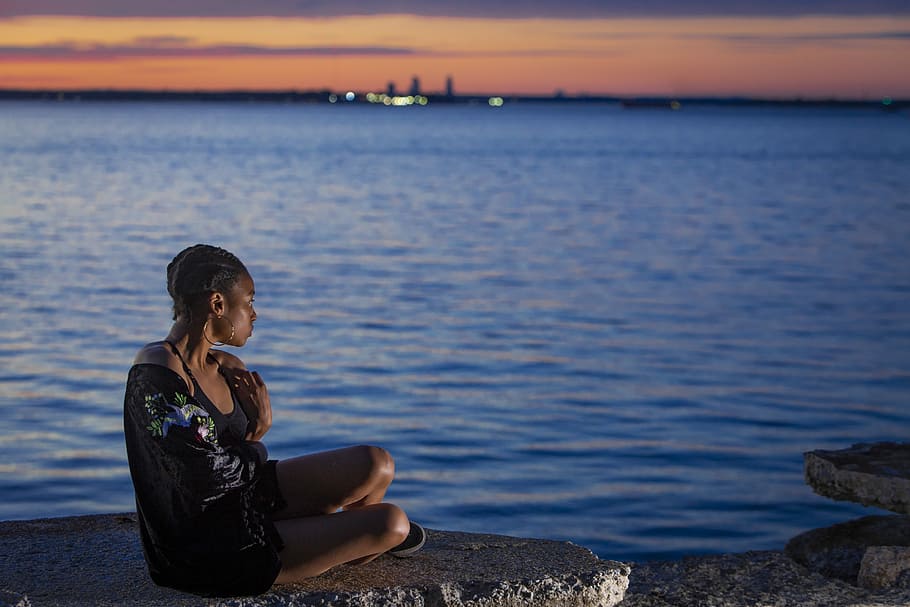 woman sitting near sea, woman sitting on gray rock groynes in front of body of water