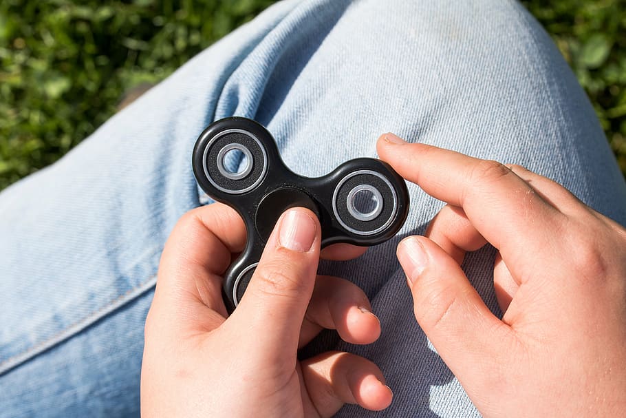 person holding black hand spinner, fidget spinner, toys, with your index finger to turn on