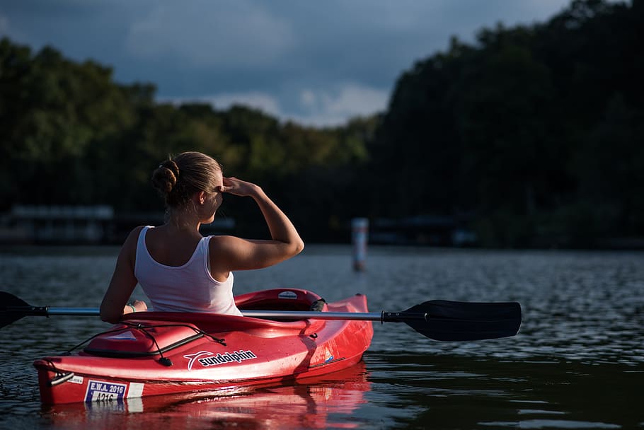 woman riding kayak holding paddle in the middle of calm body of water surrounded by trees HD wallpaper