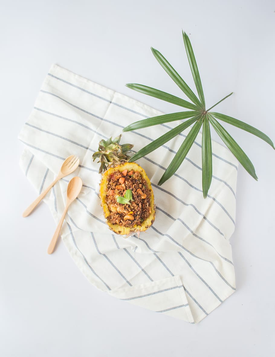 flat-lay photography of sliced pineapple, leaf, two spatulas on blanket