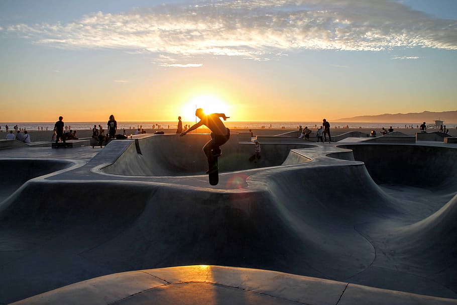 silhouette photo of man riding skateboard on skateboard ramp field, silhouette of man riding skateboard taken at sunset