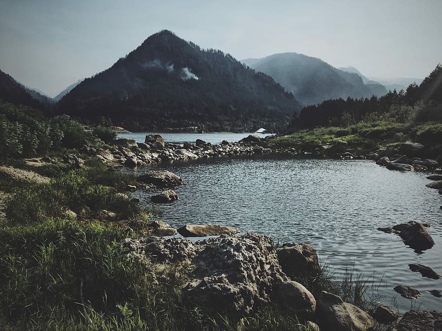 body of water surrounded by mountains, landscape photography of rocky body of water near green mountain HD wallpaper