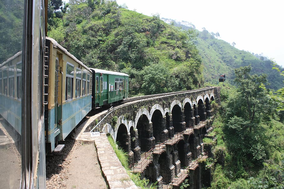 green train passing on brown arch bridge, india, shimla, kalka