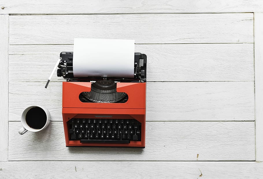 red and black typewriter beside mug on table, keyboard, coffee