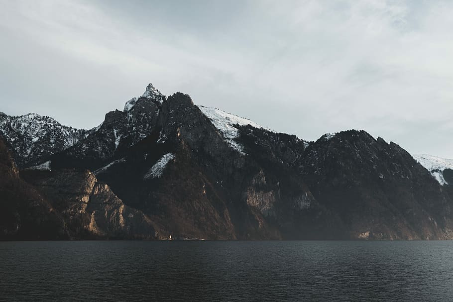 brown rocky mountains under white clouds, photo of body of water near mountains covered with snow HD wallpaper