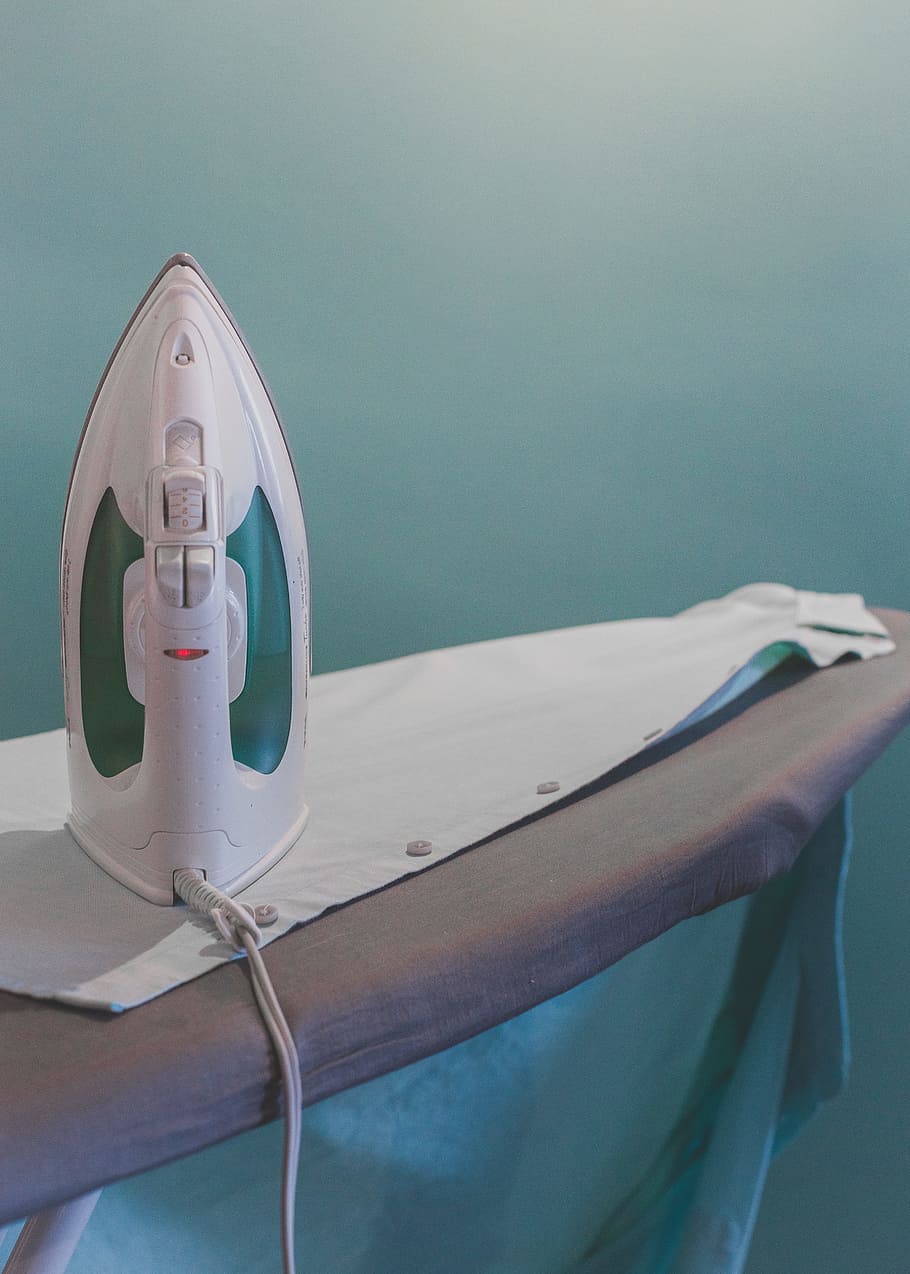 white and teal steam clothes iron plugged on ironing board, white clothes flat iron on white dress shirt