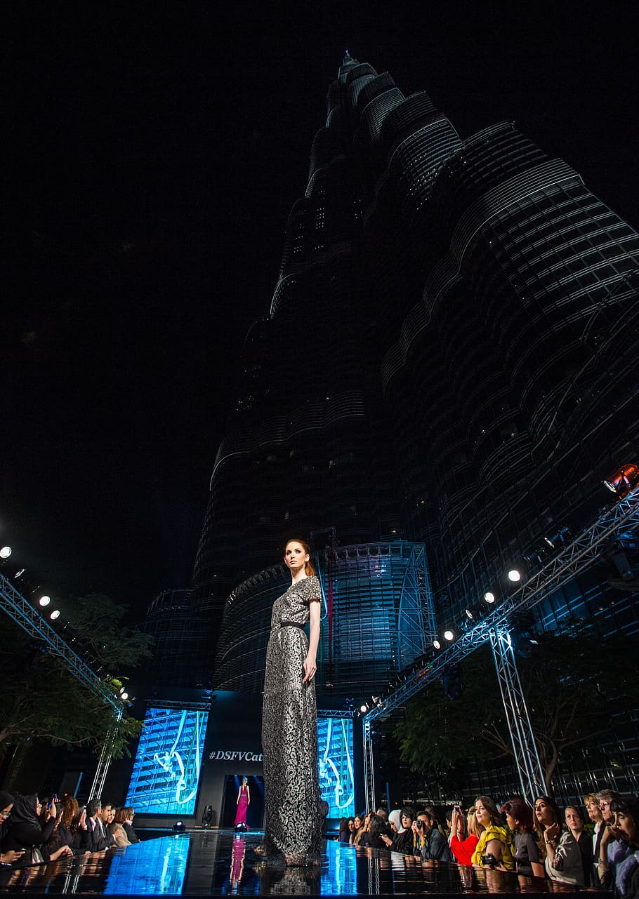 woman standing on stage beside Burj Khalifa at night time, Fashion Show