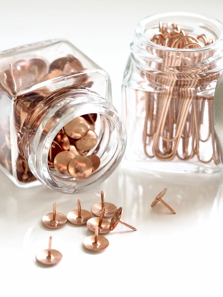 photo of bronze-colored thumb tacks and paper clips in clear glass bottles, close-up photography of brass-colored thumb tacks