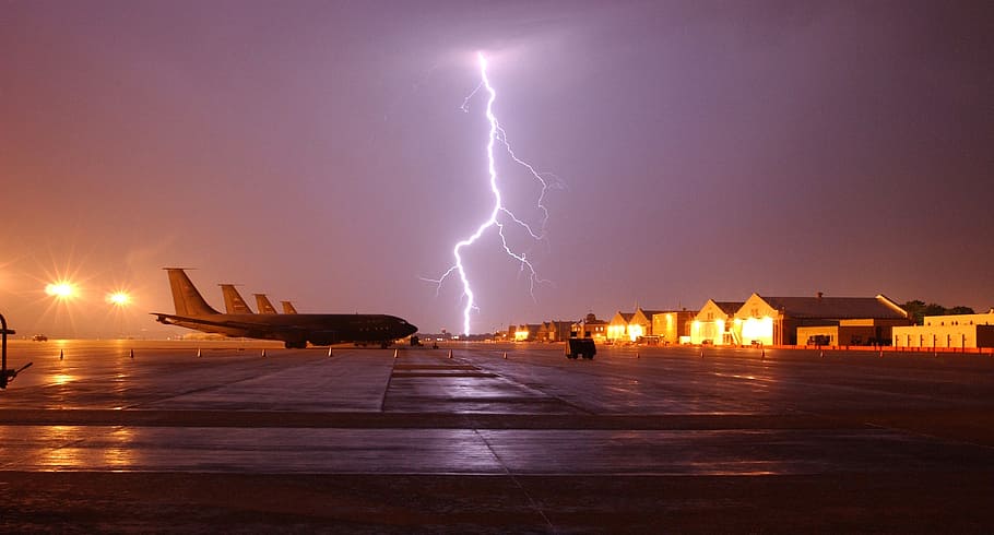 airplane parked on concrete road with lightning thunder during nighttime