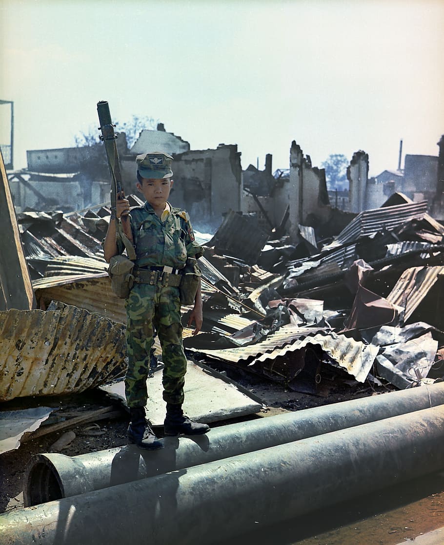 boy holding rifle standing at battleground, young child, sad