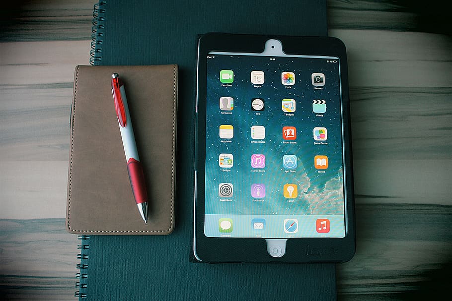 white iPad with black case on green notebook, tablet, office HD wallpaper