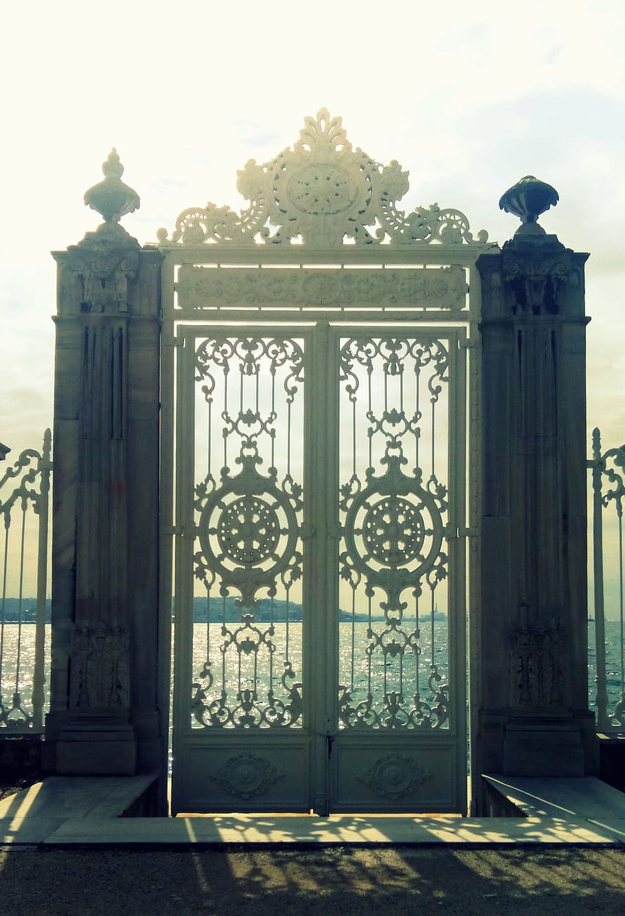 gray wrought iron gate in front of body of water, heaven, sun