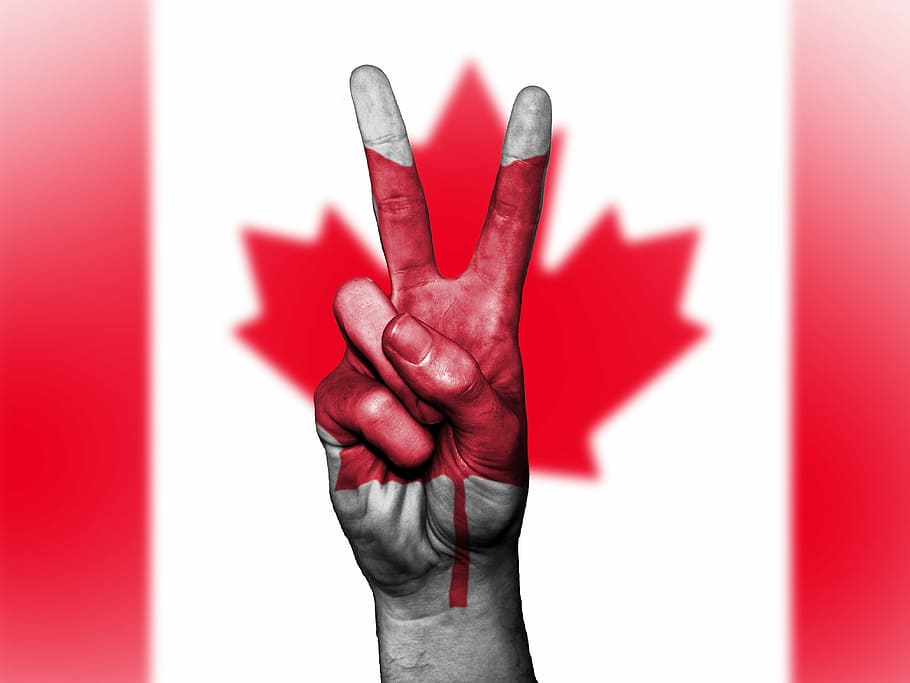 person's right hand forming peace symbol with Canada flag background