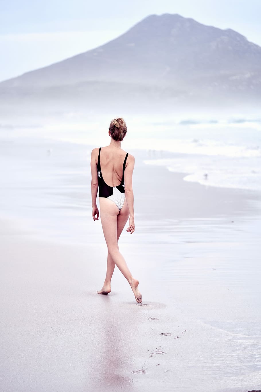 woman in one-piece swimsuit walking on seashore, woman wearing black and white one-piece swim suit