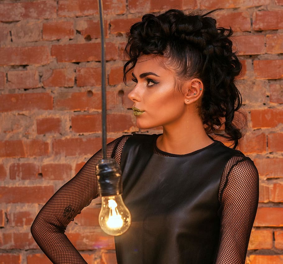 woman standing near brown brick wall with turned-on filament bulb HD wallpaper
