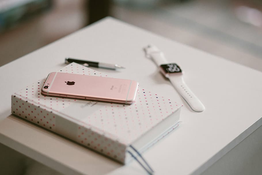 rose gold iPhone 6s on white book near gold aluminum case Apple Watch
