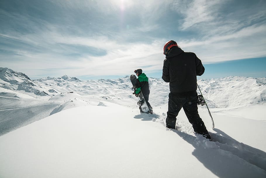 two people carrying snowboards on snow covered terrain, two men walking on ice capped field during blue sky HD wallpaper