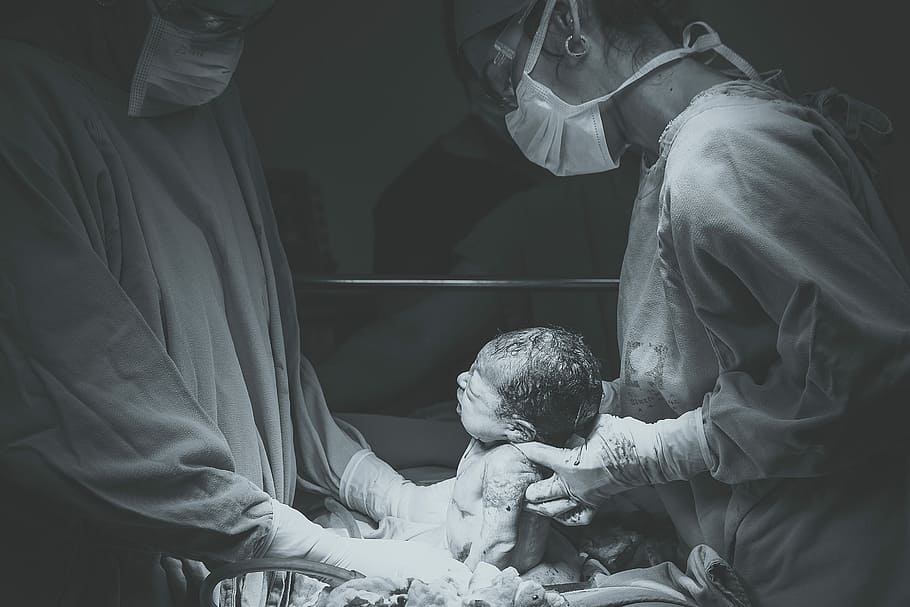 greyscale photo of medical operation, woman carrying new born baby