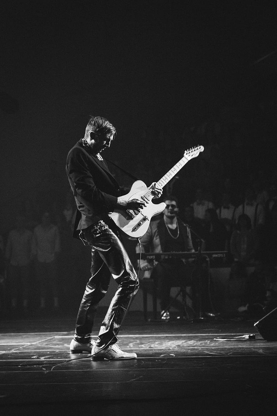 grayscale photography of man playing electric guitar near man playing electric keyboard, man holding guitar standing on stage