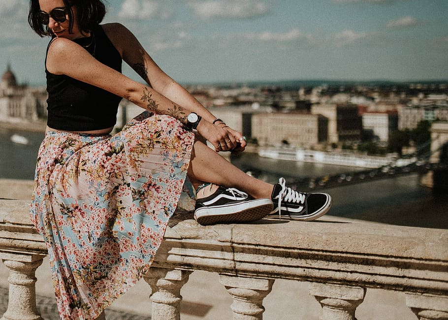 woman in sleeveless top,floral skirt and black Vans oldskool shoes, shallow focus photography of woman sitting on concrete fence HD wallpaper