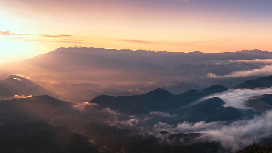 silhouette of mountain with fog at golden hour, aerial photograph of mountains surrounded with clouds HD wallpaper
