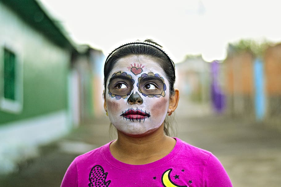 closeup photo of woman wearing pink top, woman in white and black sugar skull face mask