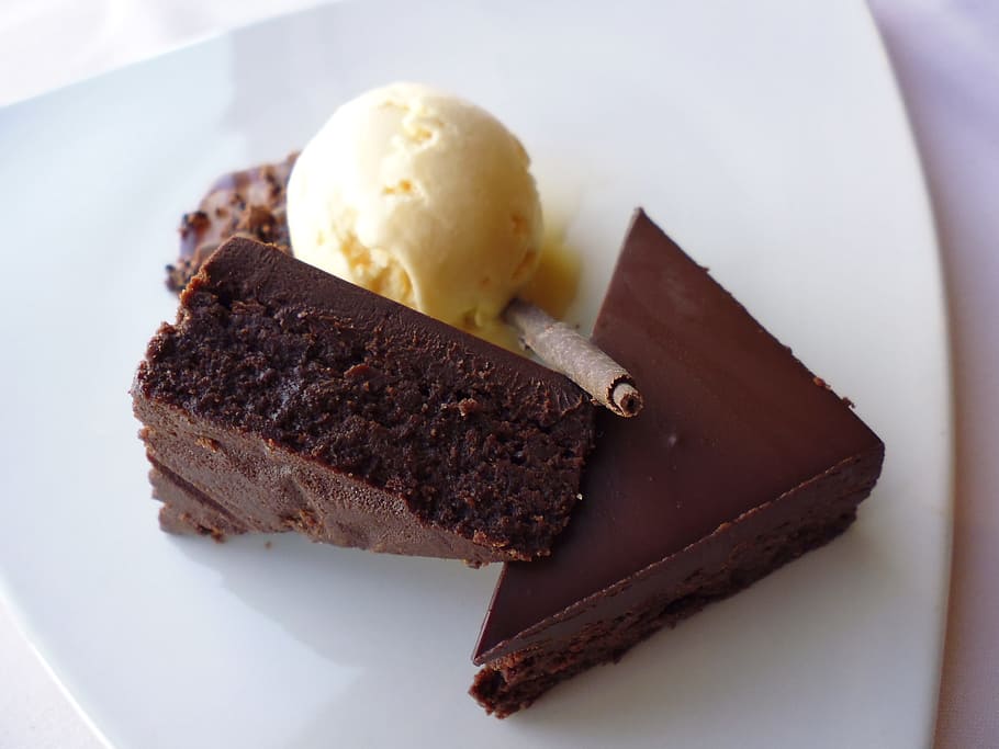 two sliced brownies beside scoop of ice cream on white ceramic plate