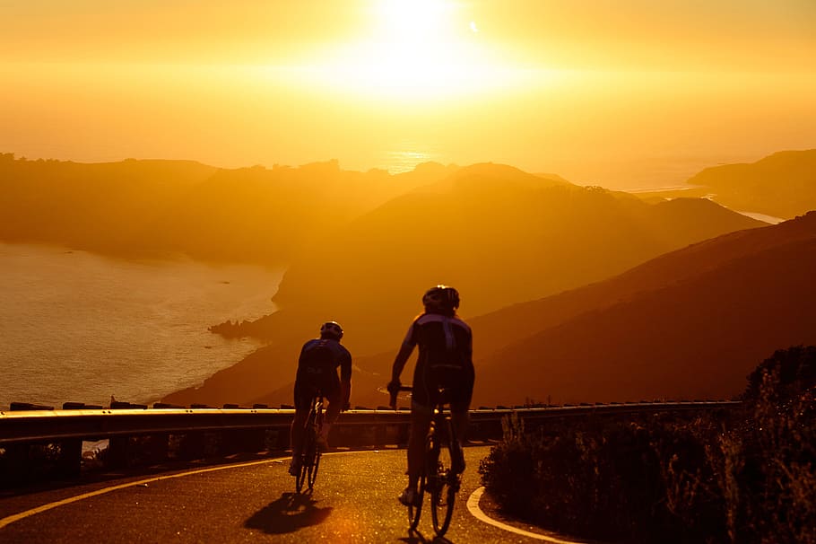 Two men on cycling exercises on bicycles on the coast at sunset, HD wallpaper