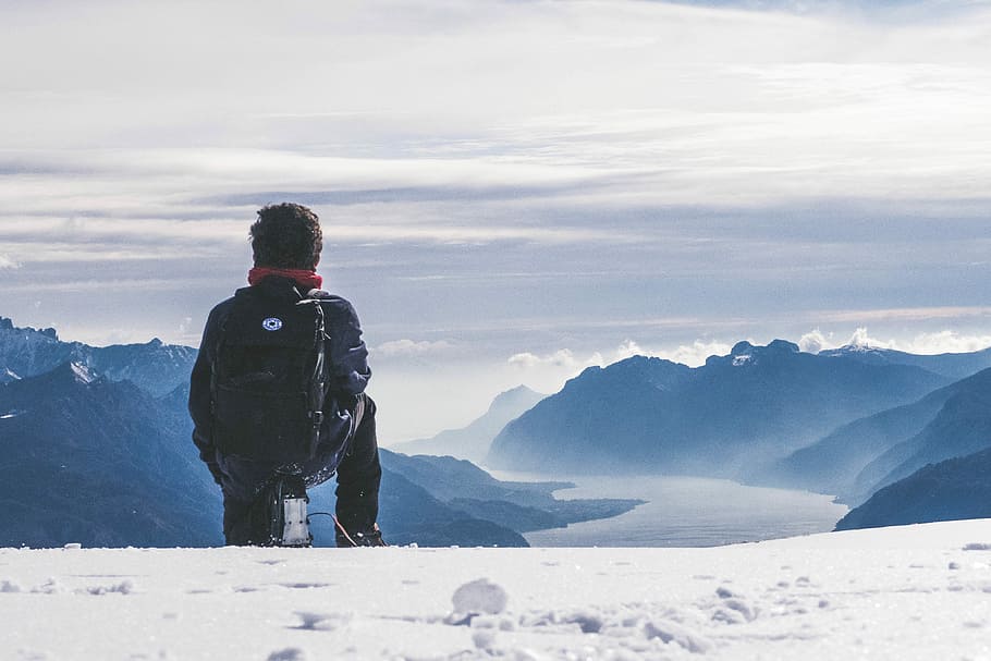 man carrying black backpack, man sitting on snow covered mountain peak HD wallpaper