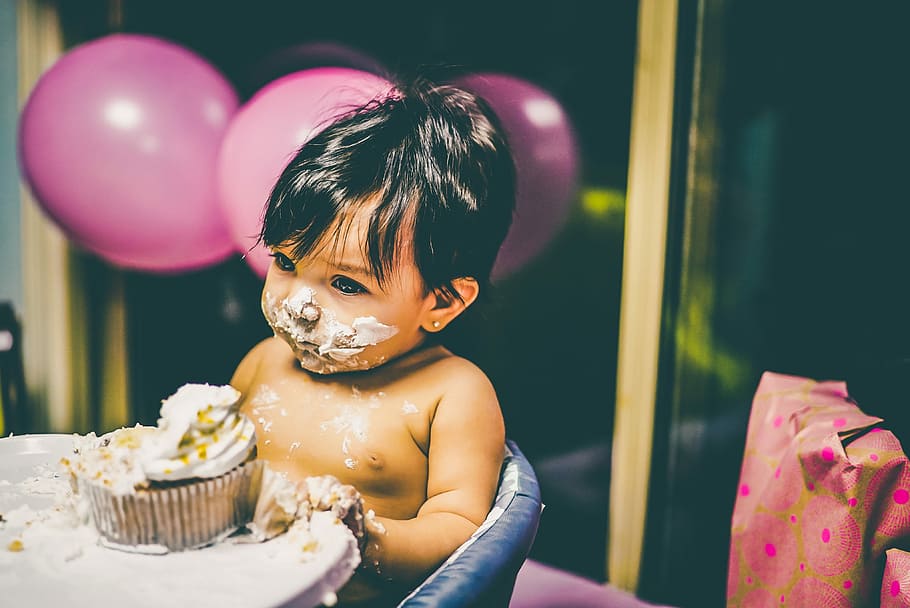 boy sitting on blue highchair, shallow focus photography of baby eating cupcake