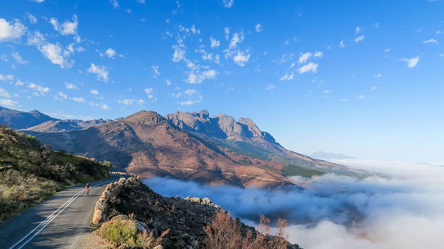 landscape photography of mountain, gray concrete road top near brown mountain and white clouds during daytime HD wallpaper