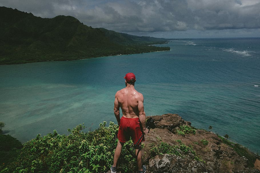 man standing on top of clipp watching body of water during daytime, man standing on edge of cliff at sea HD wallpaper